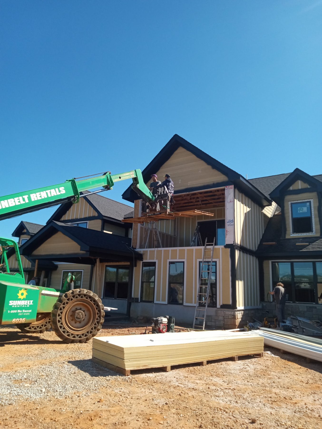 Exterior siding and finishing work on a building using a telehandler lift
